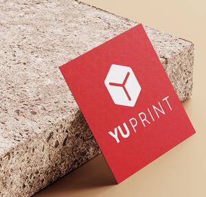 Tarjeta cuadrada roja con logotipo de Yuprint apoyada sobre superficie de piedra.