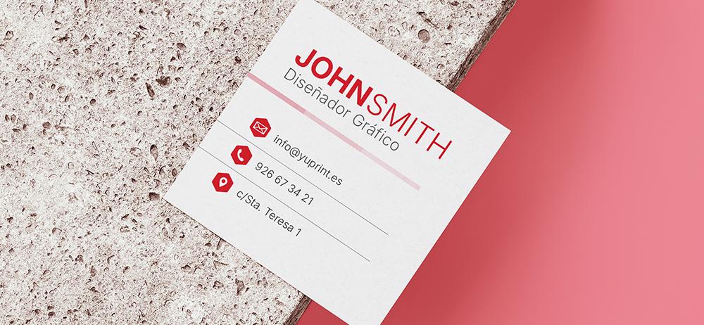 Tarjeta de presentación cuadrada en blanco y rojo sobre bloque de piedra con fondo rosa.