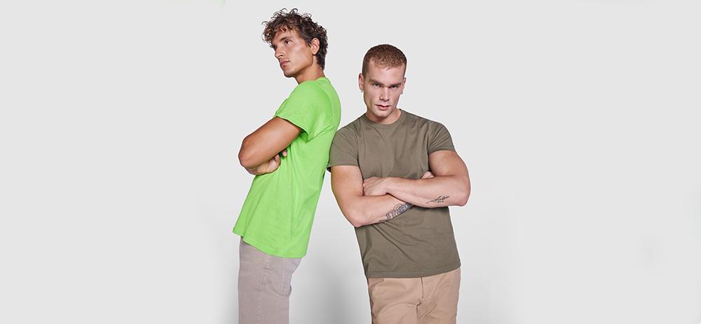 Dos modelos con camisetas verde neón y verde oliva posando espalda con espalda sobre fondo claro.